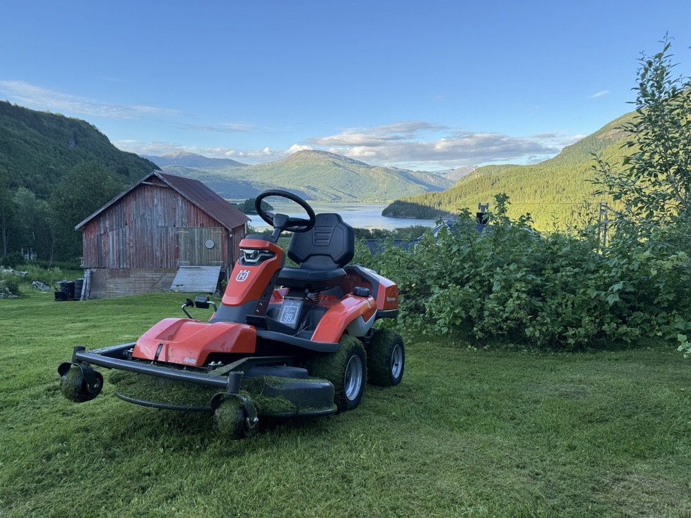 Gressklipper i utemiljø med vann og fjell i bakgrunnen